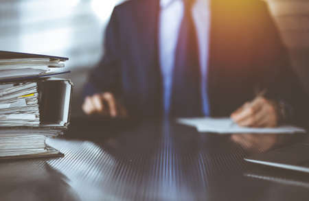 Binders with papers are waiting to be processed by unknown man accountant in blue blazer staying at home during  pandemic. Taxes and audit conceptの写真素材