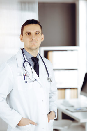 Male doctor standing straight in sunny clinic. Perfect medical service in hospitalの写真素材