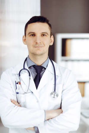 Male doctor standing straight in sunny clinic. Perfect medical service in hospitalの写真素材