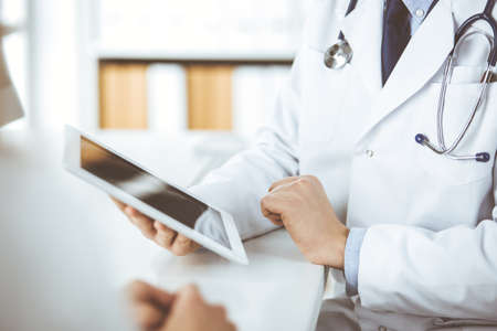 Unknown male doctor and patient woman discussing current health examination while sitting in clinic and using tablet computer. Perfect medical service in hospital. Medicine and healthcare conceptの写真素材