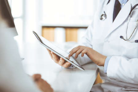 Unknown male doctor and patient woman discussing current health examination while sitting in clinic and using tablet computer. Perfect medical service in hospital. Medicine and healthcare conceptの写真素材