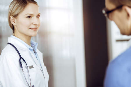 Friendly female doctor and patient man discussing current health examination while sitting in sunny clinic. Perfect medical service in hospitalの写真素材