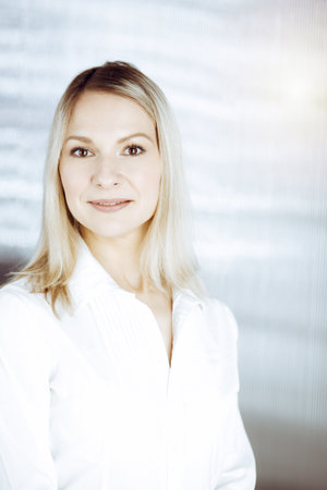 Friendly adult business woman standing straight. Business headshot or portrait in sunny officeの写真素材