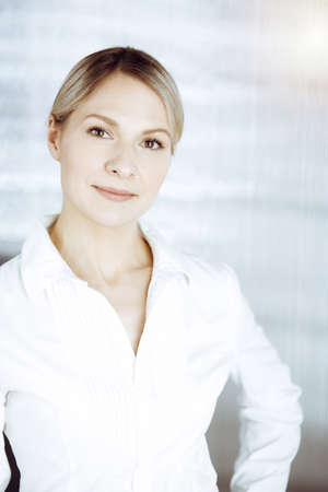 Friendly adult business woman standing straight. Business headshot or portrait in sunny officeの写真素材