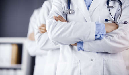 Group of modern doctors standing as a team with arms crossed in sunny hospital and ready to help patients. Medical help, insurance in health careの写真素材