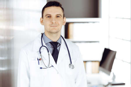 Male doctor standing straight in sunny clinic. Perfect medical service in hospitalの写真素材