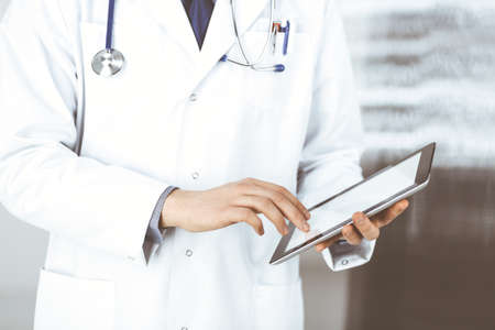 Unknown male doctor using tablet computer in clinic near his working place, closeup. Perfect medical service in hospital. Medicine and healthcare conceptの写真素材