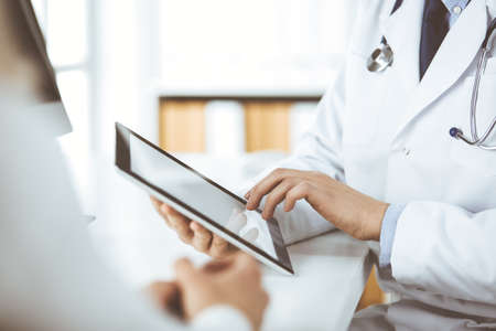 Unknown male doctor and patient woman discussing current health examination while sitting in clinic and using tablet computer. Perfect medical service in hospital. Medicine and healthcare conceptの写真素材