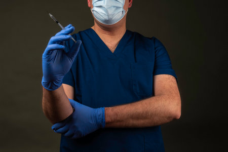 doctor in blue scrubs and mask with syringe on dark background