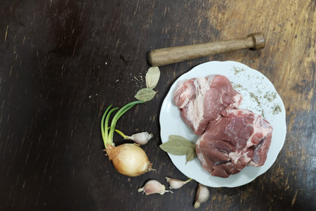 Raw pork neck with garlic, onion and bay leaf on wooden backgroundの写真素材