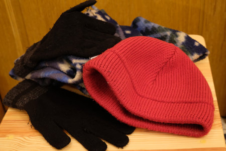 Woolen gloves and a red hat on a wooden shelf.