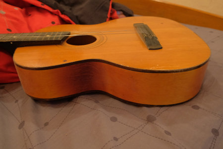 Old classical guitar on a bed in a brown apartment lying on a blanket of red productsの写真素材