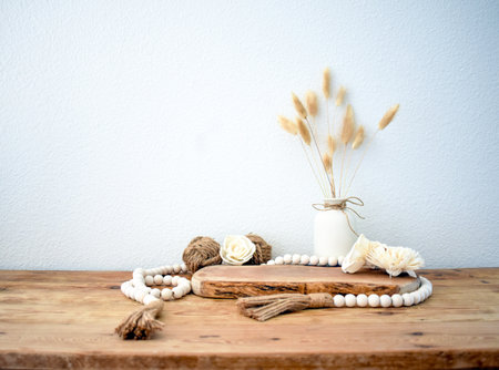 Stylish composition of table with beads and flowers and crown, bench in retro style, clay vases and crockery. Rustic inspiration. Summer vibes. Beige wood table.の写真素材