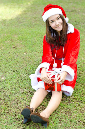 A Smiley Asian santa woman with box gifts sit on green field  の写真素材