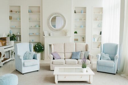 Classic living room in blue and white shades. Sofa, armchairs, fireplace, coffee table and mirror in...