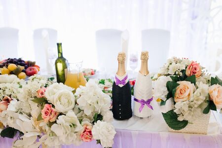 Two bottles of champagne, dressed as the bride and groom, stood on the wedding party table in flowersの写真素材