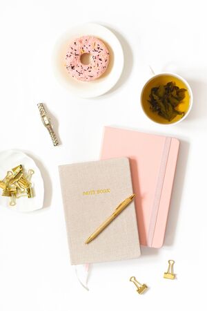 Tea break at the workplace of a freelancer or female blogger. Donat, tea in a mug, notebooks, pen on a white background. Trend background for the blogの写真素材