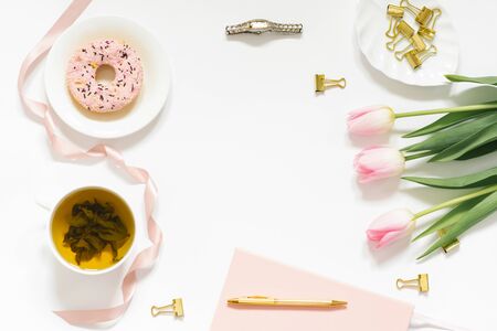 Stylish flat lay for a woman's fashion blogger. Workplace of a freelancer or office worker: a pink-covered diary, a pen, a Cup of green tea, a pink donut, a bouquet of pink spring tulips. A trending concept with space to copyの写真素材