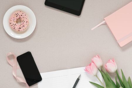 Trendy stylish frame for a female blogger, freelancer: pink diary, tablet, phone, Donat on a plate, pink tulips and an open Notepad with a clean page on a coffee background with copy space. Working from home placeの写真素材