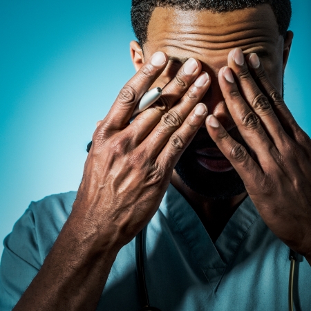 Studio shot of a young African American doctor suffering fatigue and rubbing his eyes の写真素材