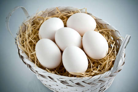 Bunch of whole white eggs on a nest of straw in a white basket made of wicker
