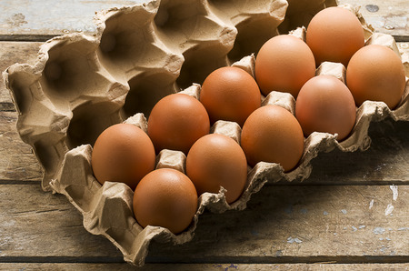 Ten whole brown eggs in a cartoon container open on rustic wooden table