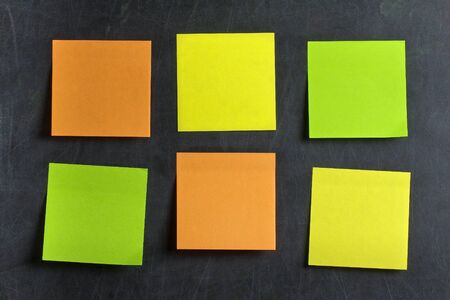 Blank Green orange and yellow postits glued on blackboard or chalkboard