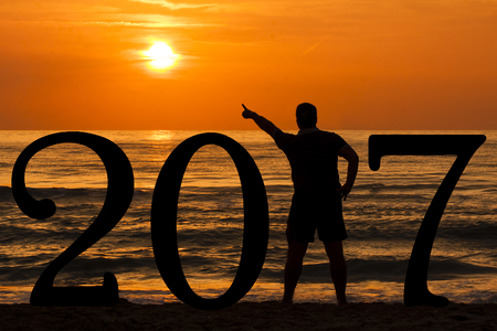 Man Silhouette forming year 2017 pointing out sun at sunrise at sea