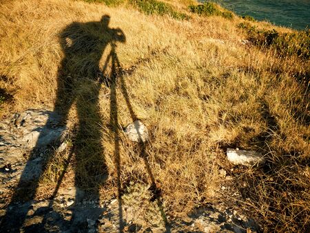 Silhouette of male photographer taking shot with tripod at seasideの写真素材