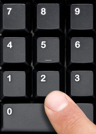 Top view of black computer keyboard numeric keys that are about to be pressed by male finger