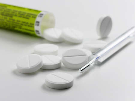white pills or tablets spilling out of pill bottle and thermometer