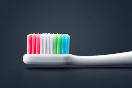 A close-up view of a colorful toothbrush featuring vibrant bristles in pink, blue, and green. The toothbrush is set against a dark background, highlighting its design and colors. ai generated.の素材