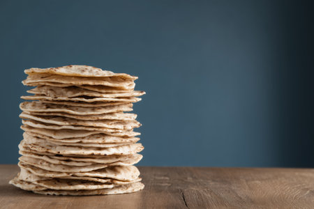 A tall stack of flatbreads is displayed on a rustic wooden table against a blue background. This image captures the texture and layers of the flatbreads, making it ideal for food-related themes. ai generated.の素材