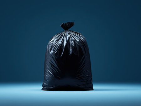 A black garbage bag stands upright against a solid blue background. The image highlights the simplicity and functionality of waste disposal in a clean and modern setting. ai generated.の素材