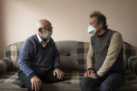 An elderly and a senior man wearing masks chatting about covid19 in their homeの写真素材