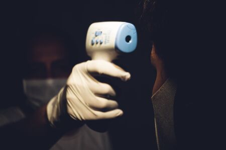 Senior healthcare worker measuring a young adults body temperature with infrared thermometer to test...