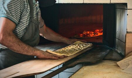 Turkish Muslim baker chef putting traditional ramadan bread of turkish cuisine into the oven in...