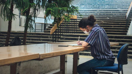 Left angle Isolated long haired and masked young university student studying alone in the libraryの写真素材