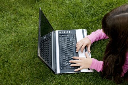  Young beautiful girl lying on grass at park and using laptop