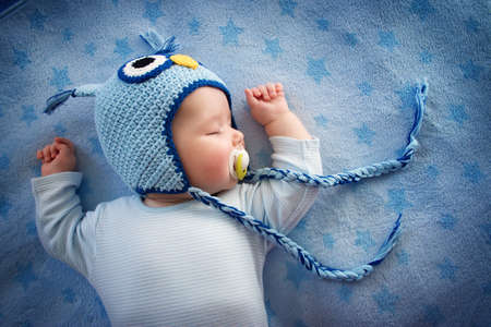 4 month old baby in owl sleeping on blue blanketの写真素材