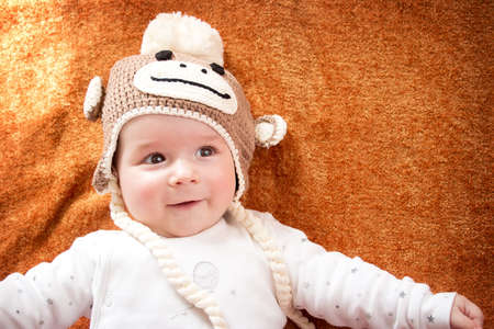 little baby in knitted montey hat on brown blanket