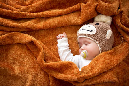 little baby in knitted montey hat on brown blanket