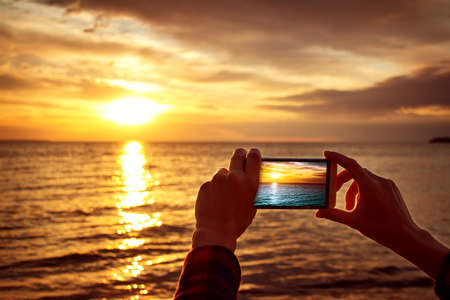 woman hands holding mobile phone at sunsetの写真素材