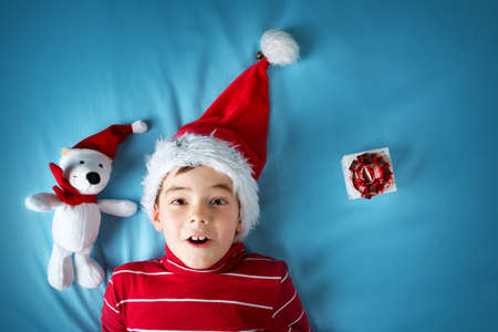 Happy boy in santa claus hat with a white bear on blue blanketの写真素材