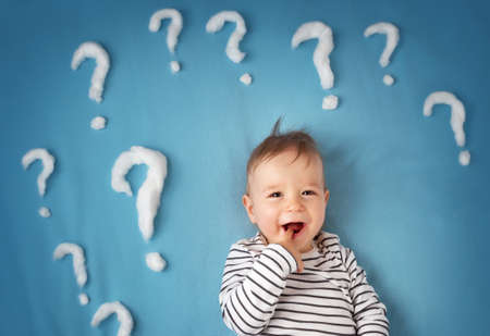 funny little boy lying on blue blanket with lots of question marksの写真素材