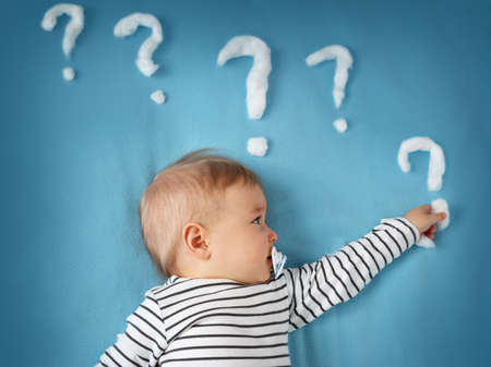 funny little boy lying on blue blanket with lots of question marksの写真素材