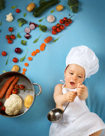 Baby boy in chef hat with cooking pan and raw vegetablesの写真素材