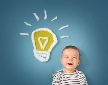 One year old boy with a bulb on blue background. Child with an ideaの写真素材