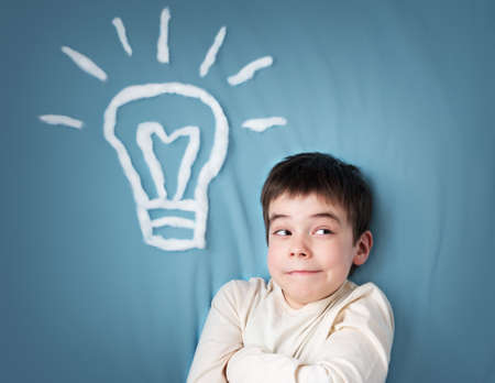 seven years old boy with a bulb on blue background. Child with an ideaの写真素材