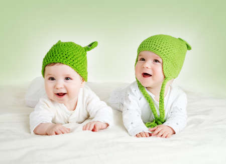 two cute six month old babies lying in frog hats on soft blanket